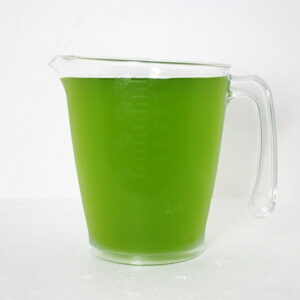 Clear glass measuring pitcher filled with bright green juice on a white surface.